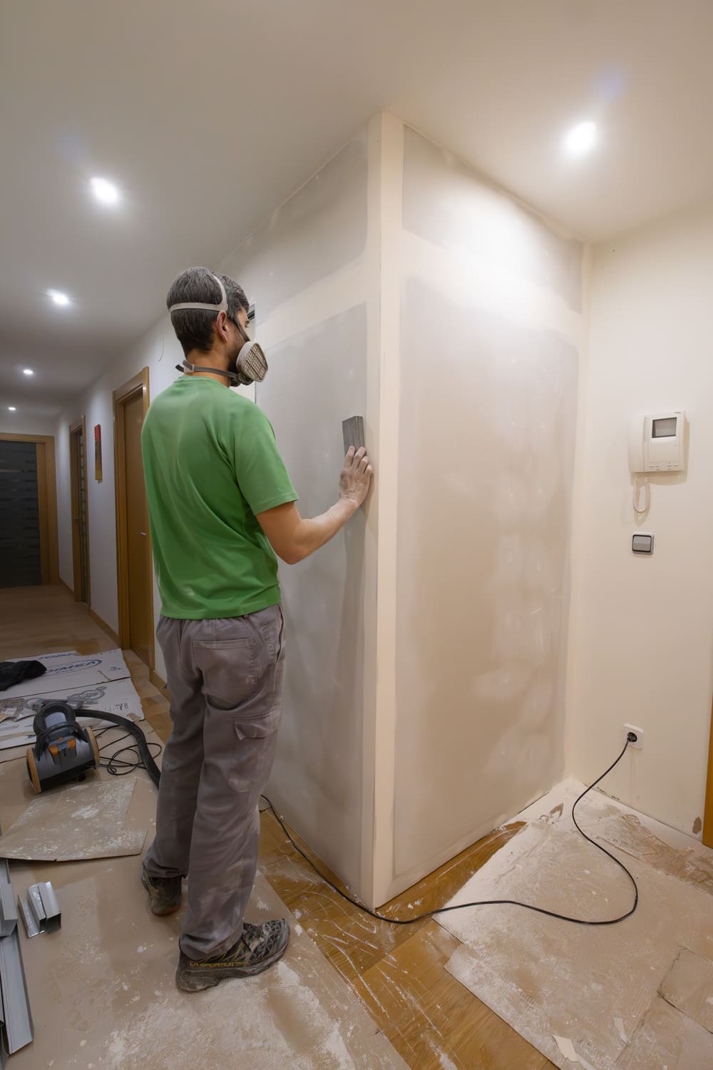 tired-man-works-home-sanding-drywall-wall-with-dust-mask-powdered-housework